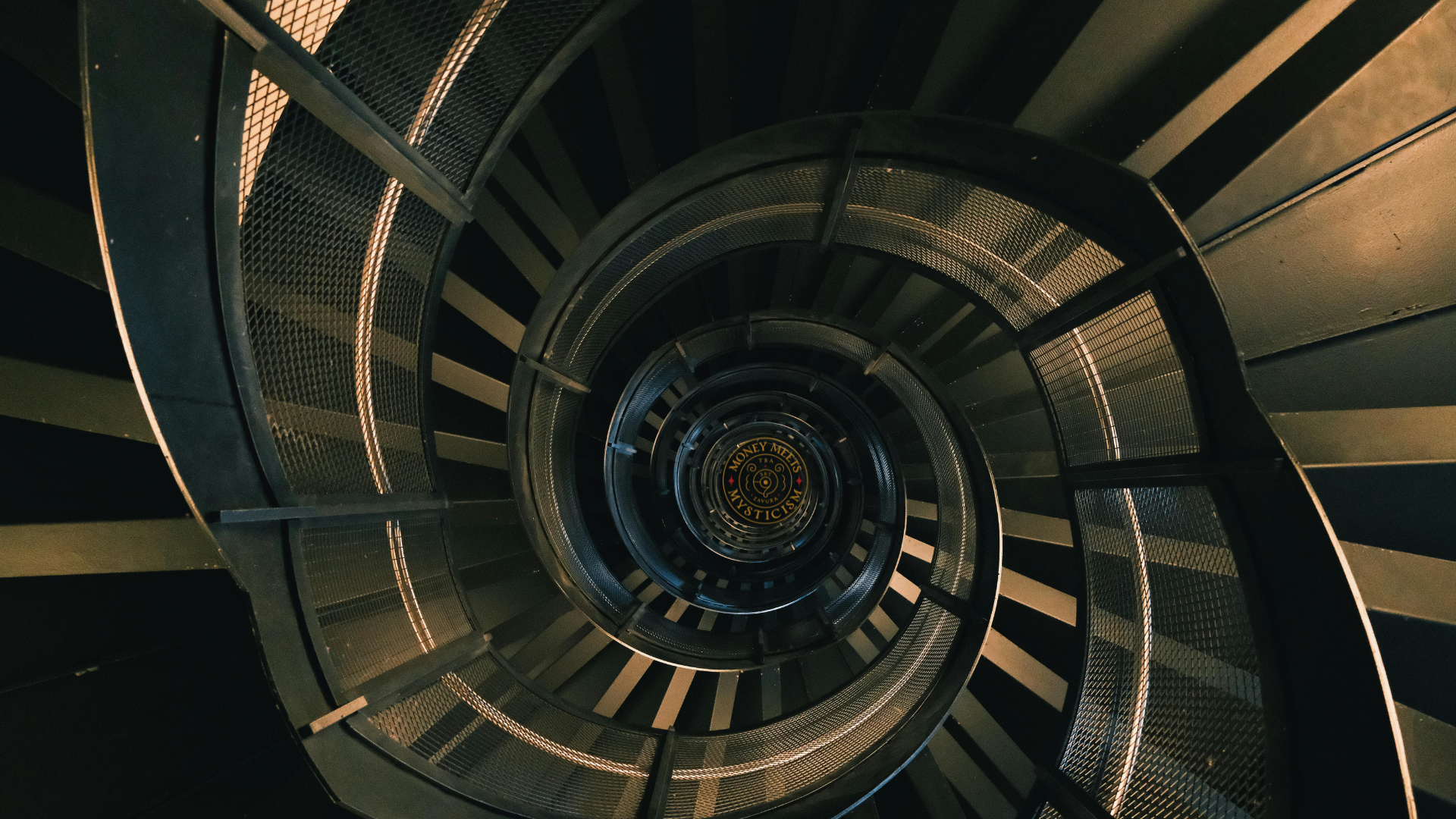 A dark industrial spiral staircase descending to the studio&rsquo;s seal.